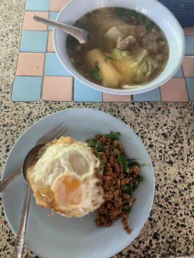 a bowl containing an egg, pakaprow, and rice alongside another bowl of soup