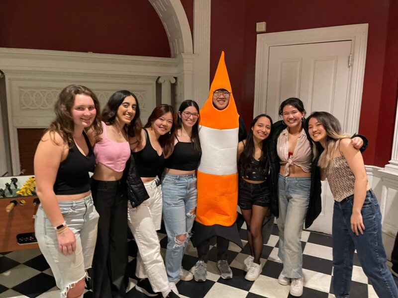 group of people smiling with one person dressed as a traffic cone in the middle