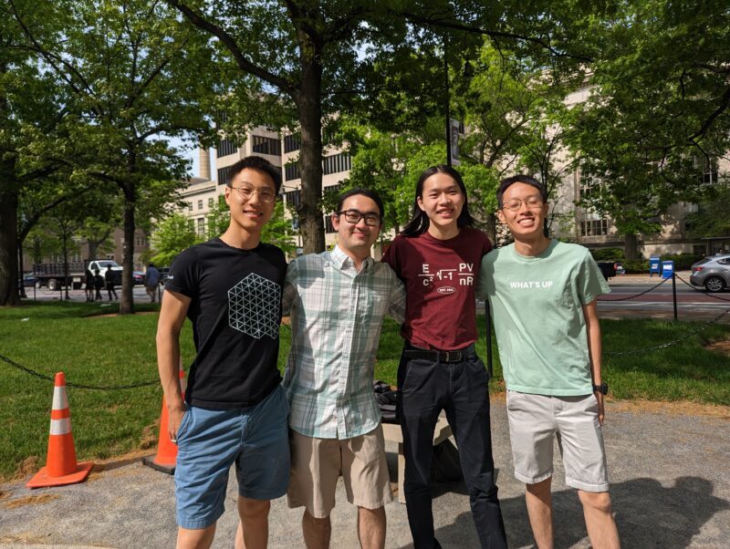 four college students in a line in front of a lawn and some trees