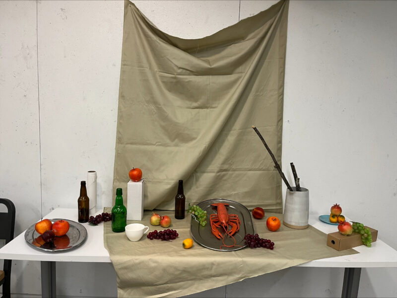 table with drape and various fruit, bottles, and other items placed on it