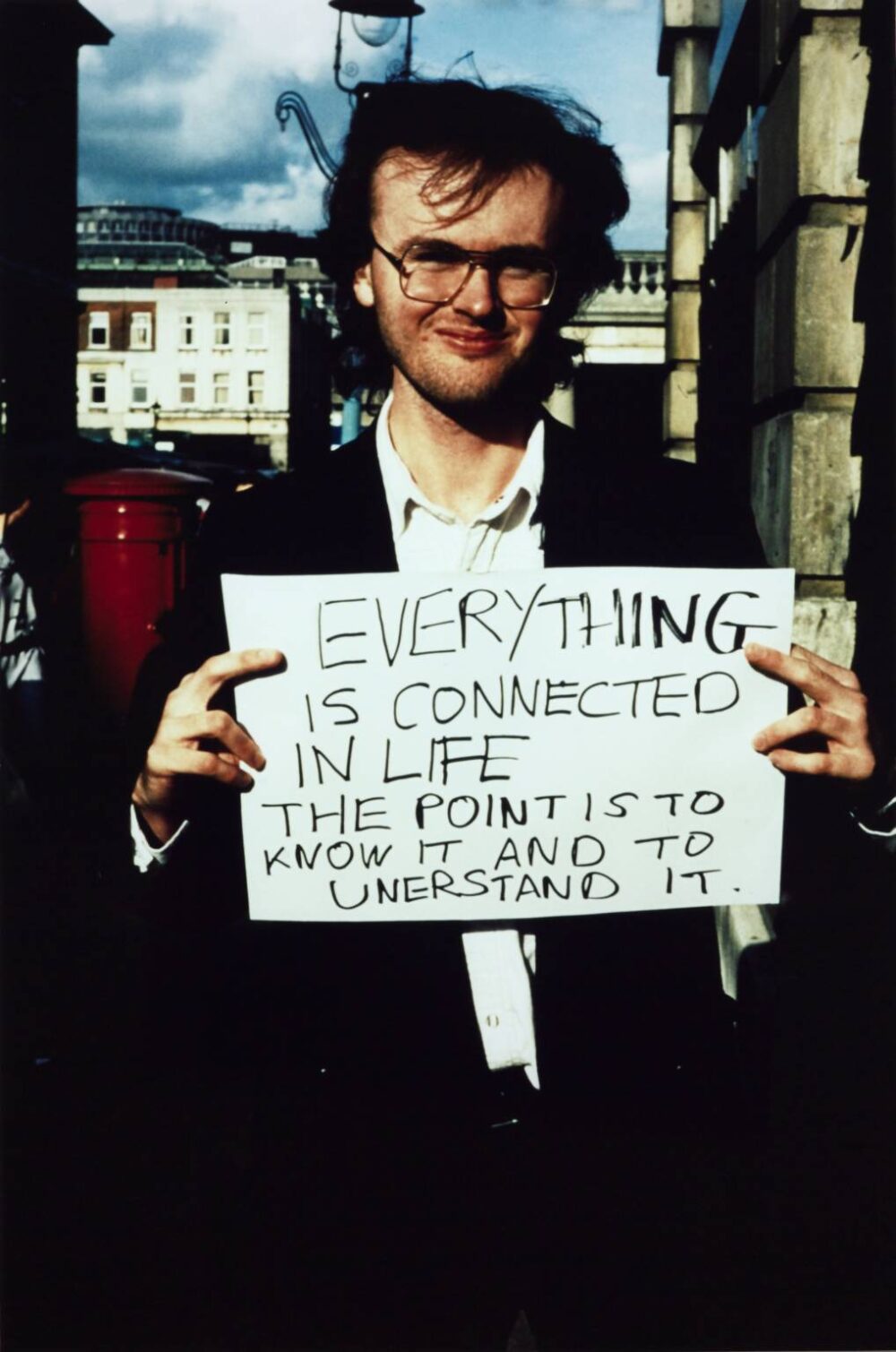 man holding up sign that reads "everything is connected in life. the point is to know it and to understand it."