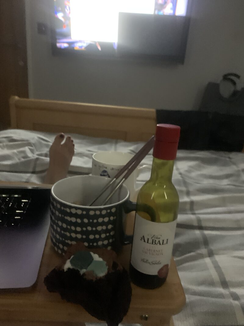 wine, cup of a tea, and a chocolate cake on a lap table while i lay in bed watching tv