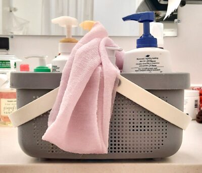 Grey shower caddy w/ white handles, filled w/ toiletries and sitting on a bathroom counter