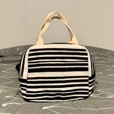 Black & white striped lunch bag sitting on a grey bed spread