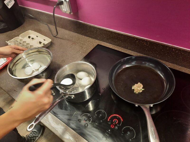 Eggs being transferred from a pot to a bowl, plus a small bit of dumpling filling in a pan