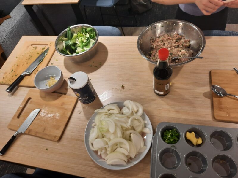 Two cutting boards & knives, and onions, bok choy, garlic, and dumpling filling all in different bowls.
