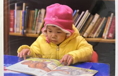 Image of baby in library at table reading a children's book.
