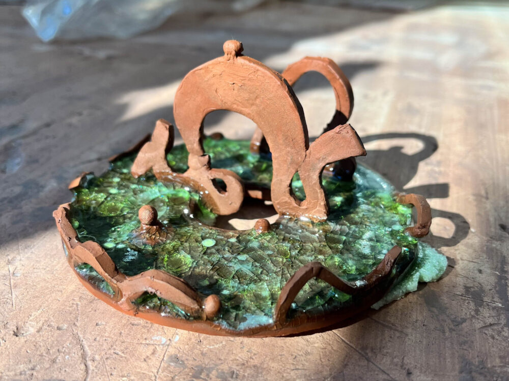 a picture of a circular clay tray with thin dragon forms on top and a crackly green glass base