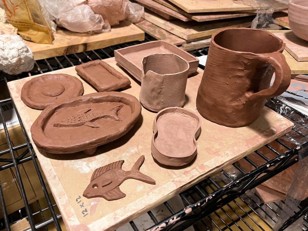picture of a wooden board with various red clay things on top, including a mug, some trays, and a small fish