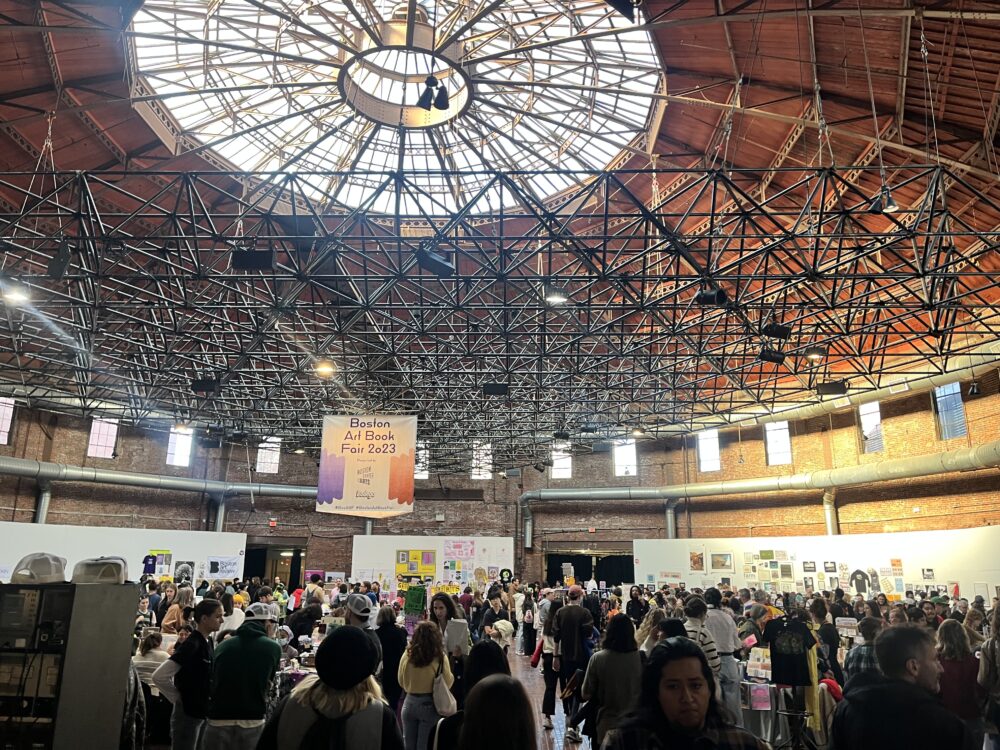 a picture of a large circular room with a domed roof. it's filled with booths, artwork, and people milling about