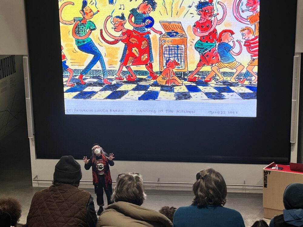 a picture of a gesturing woman in front of a large LED screen with a drawing on it