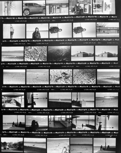 a 7x5 grid of black and white film negatives of various beach scenes, including seagulls, buildings, and portraits of a woman