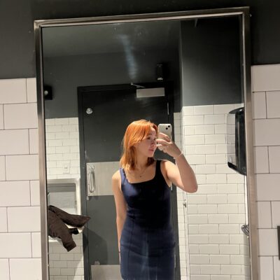 a picture of a girl taking a mirror selfie, wearing a blue dress. her hair is bright orange under the lights