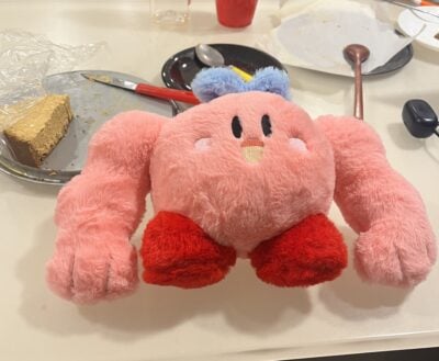 a pink kirby plush with buff arms on a table