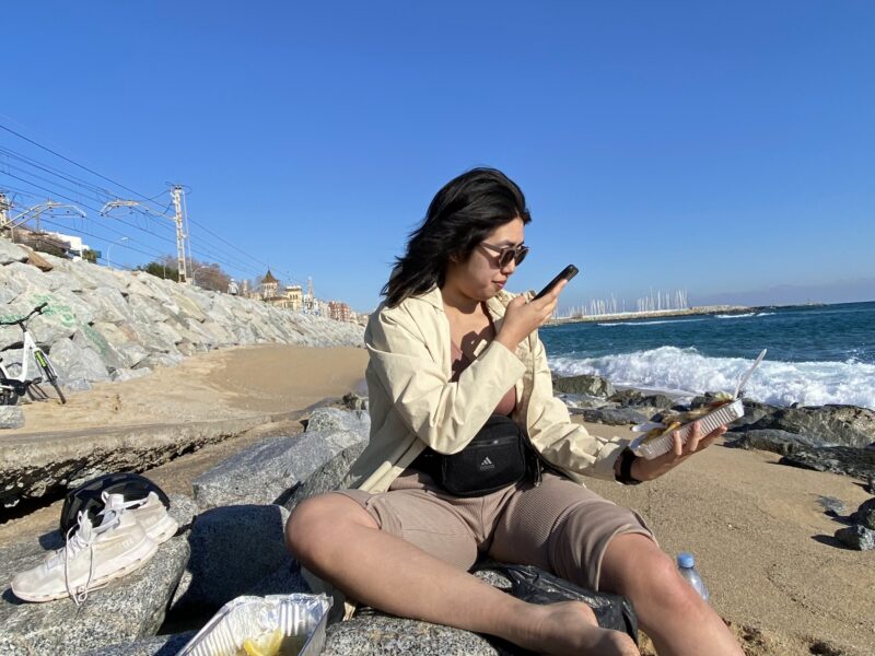 woman taking a picture of food next to the beach