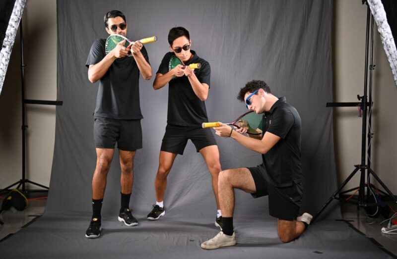 Squash team posing with rackets.