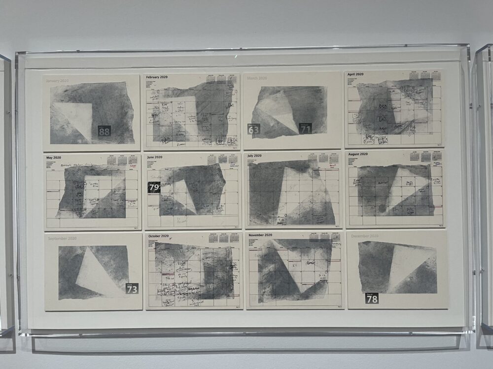 photo of a set of collages on the wall. they consist of calendars, one for each month, with swaths of ash charcoal and black stamping over them.