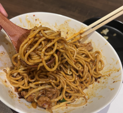Image of noodles with chili oil in a bowl. Chopsticks and spoon in bowl.
