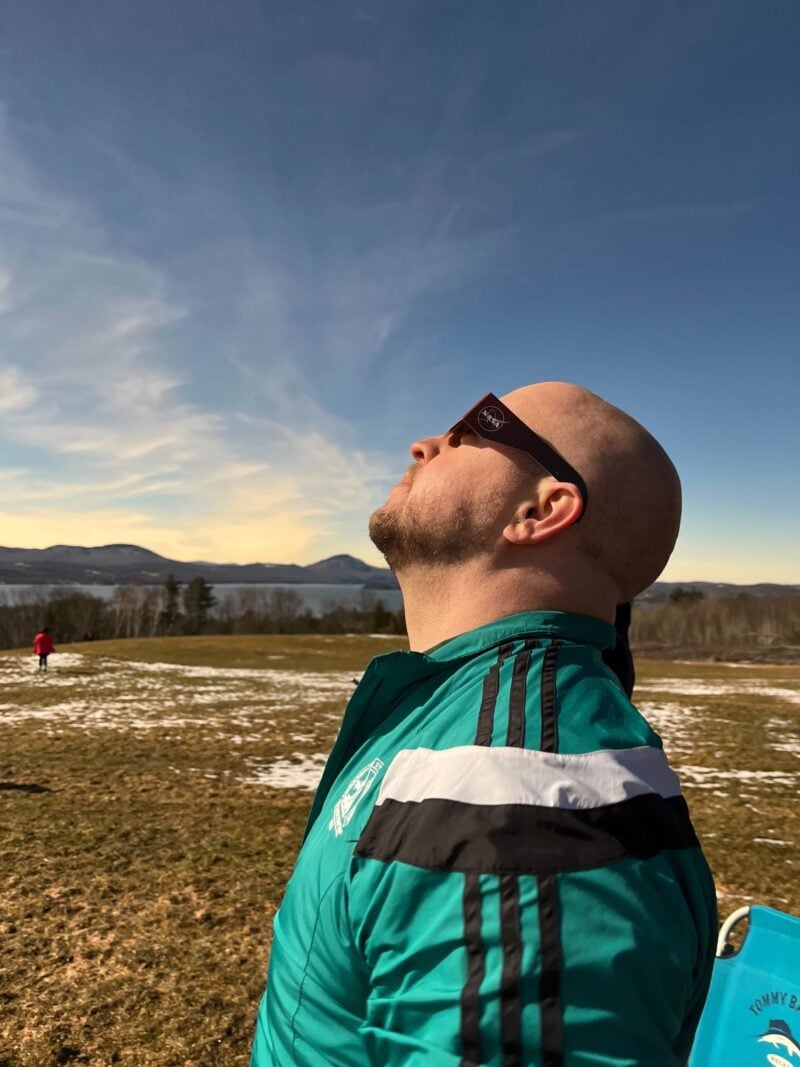 the author of the blog post wearing a windbreaker and eclipse glasses looking into the sky