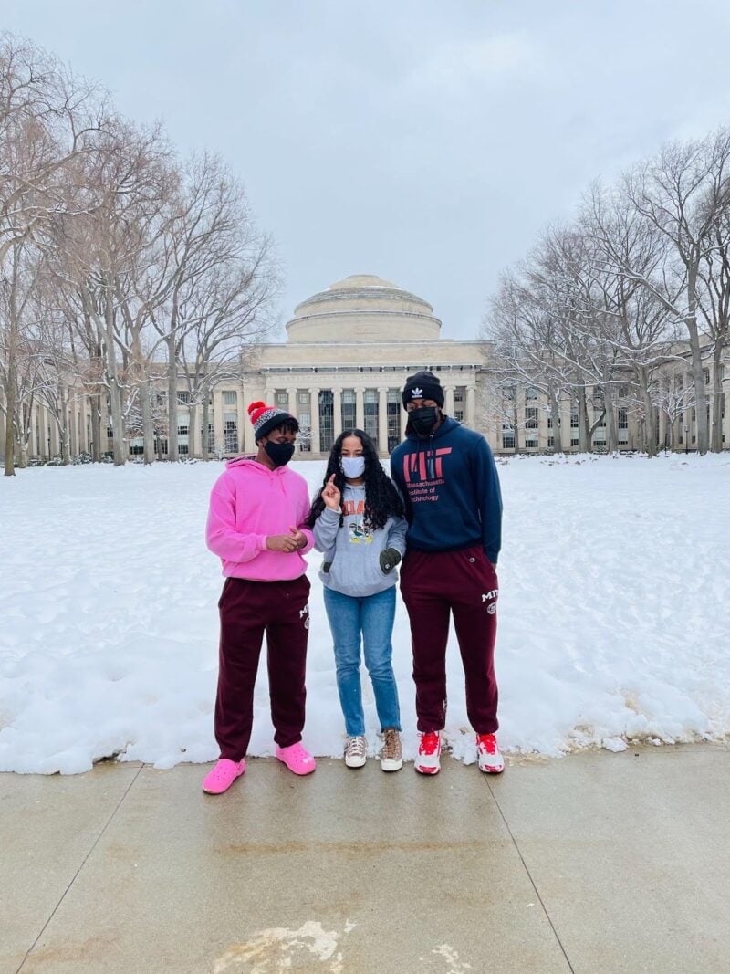 Three MIT students, wearing masks, stand in front of a snowy Killian Court and the Great Dome of MIT