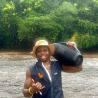 Andre standing in front of a river while it's raining, in a bucket hat and…