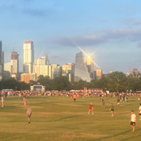 People playing in wide open park, with city skyline behind them.