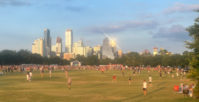 People playing in wide open park, with city skyline behind them.