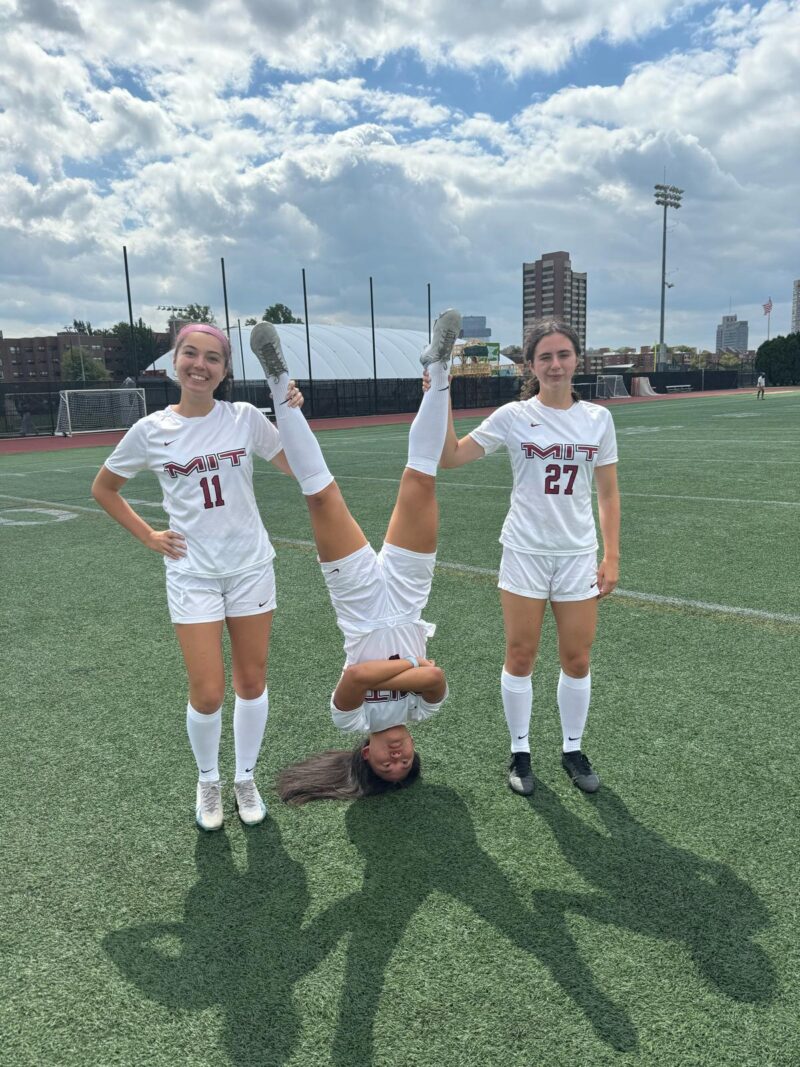 Two girls standing with a girl on her head in the middle.