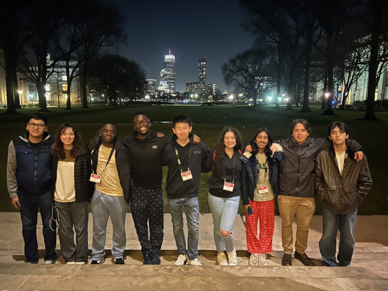 Group photo taken in front of MIT's great dome featuring the Boston Skyline in the back