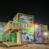 A colorful, painted with murals, lit-up three-story wooden fort. There's an LED sign that says…