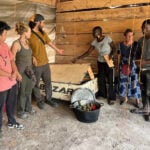 MIT D-Lab students with mentors and community partners in Cameroon, stand by their first low-cost brooder box and one load of beeswax thermal batteries.