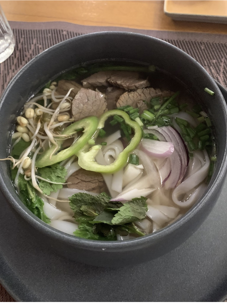 A picture of a bowl of pho. There is meat, onions, peppers, and noodles. It looks very tasty. 