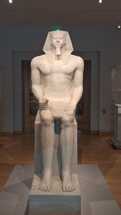 A ancient marble statue of an Egyptian figure sitting. 