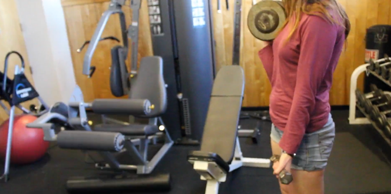 a picture of a lady curling dumbbells with other machines in the background