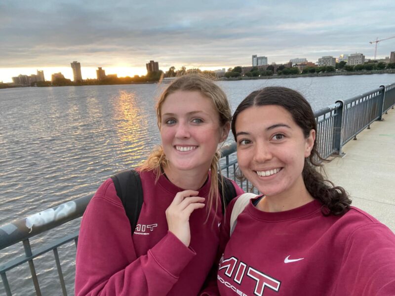 Two girls smiling next to river on bridge.