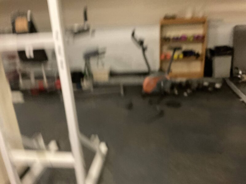 a blurry picture of a gym with some scattered machines and a shelf