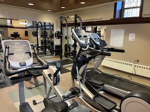 a picture of a beige room with some black fitness machines and a mirror