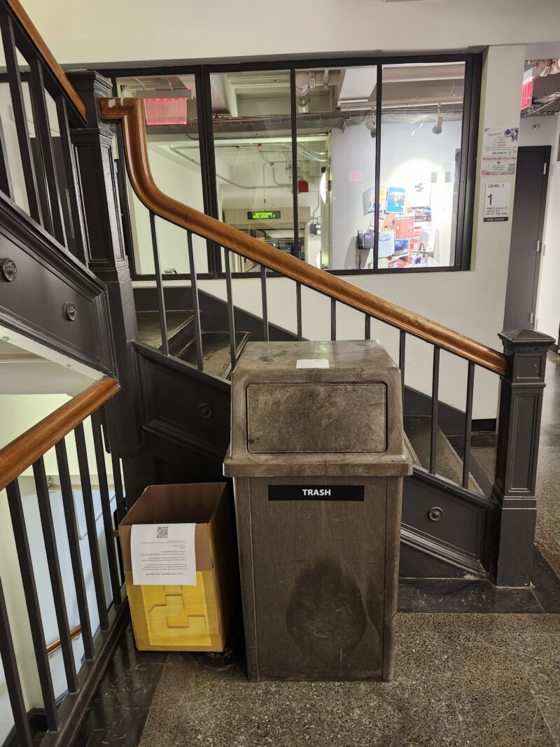 Yellow-covered box with question mark next to trash can & staircase