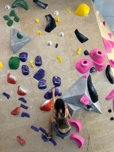 A girl climbing on a rock climbing wall, towards the bottom of the wall. 