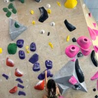 A girl climbing on a rock climbing wall, towards the bottom of the wall.