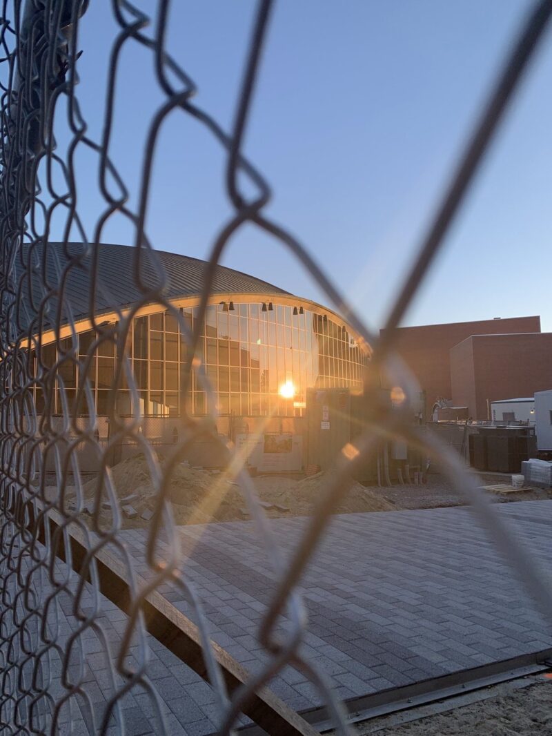 The reflection of the sun against a Kresge window seen through a chain-link fence