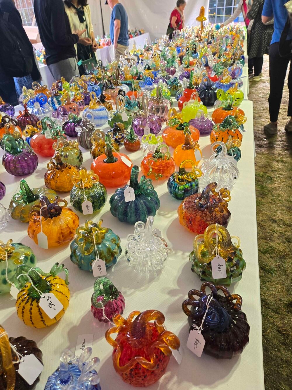 a table is filled with brightly colored glass pumpkins of different shapes and colors