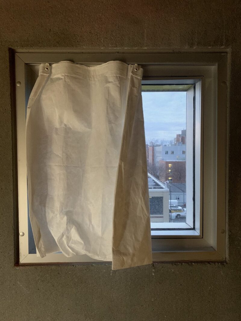 The view from a square shaped window overlooking Cambridge, half covered by a curtain.