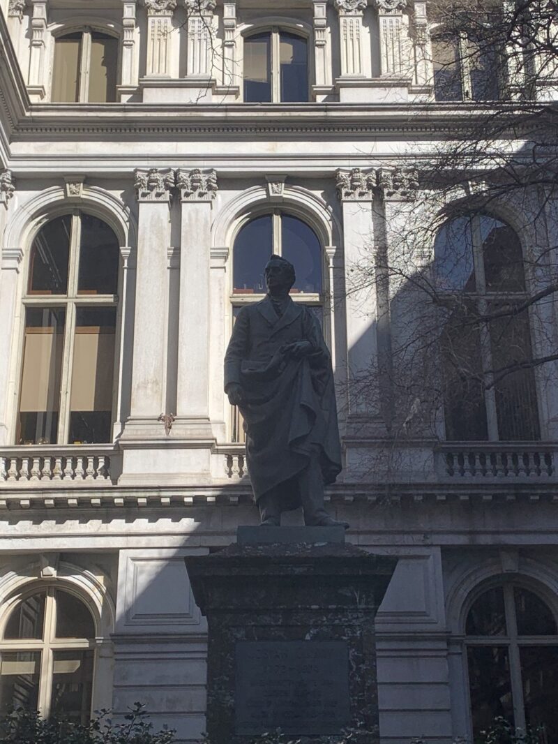 A statue in front of a historic boston building, against shadow and light