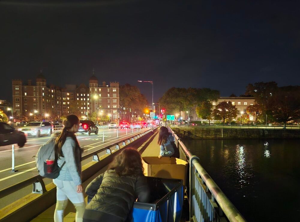 3 people pushing carts across a bridge at night