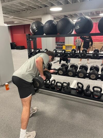 Soccer player doing rows with a weight next to a bunch of dumbbells.