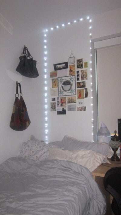 A light blue bed with blue string lights and a collage on the wall behind it.