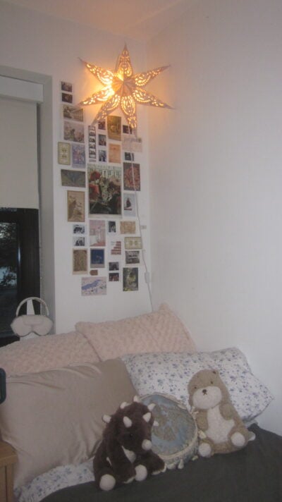 A green bed with stuffed animals and a collage on the wall behind it. There is a gold star lamp