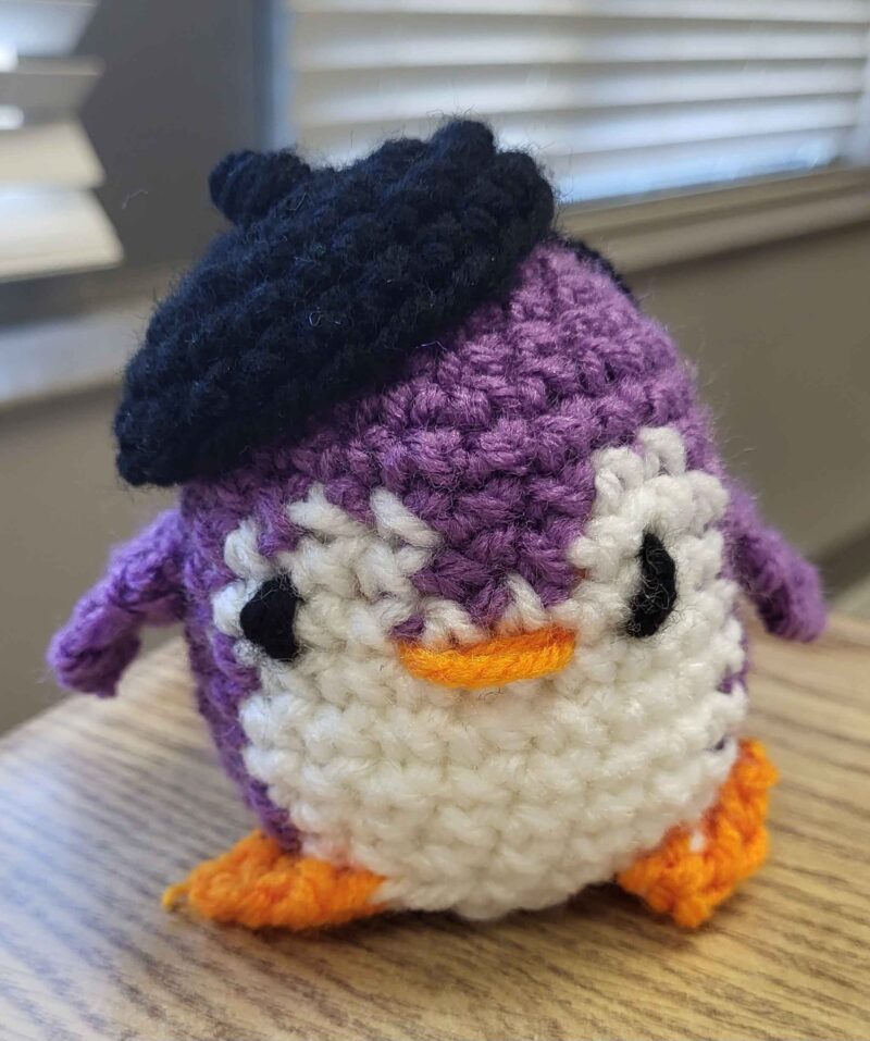 a purple crochet penguin with a beret