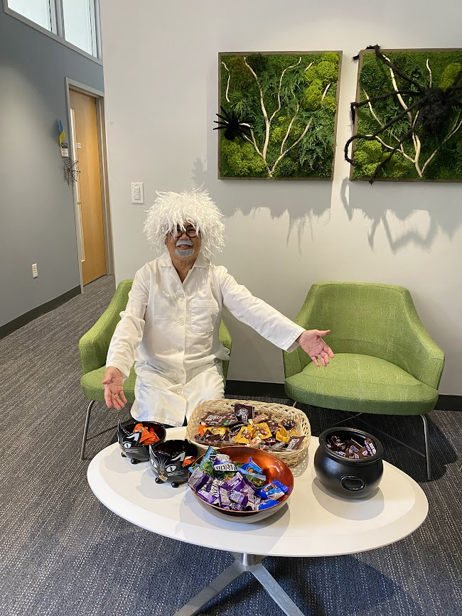 person dressed up as Einstein gesturing to a lot of candy on the table in front of them